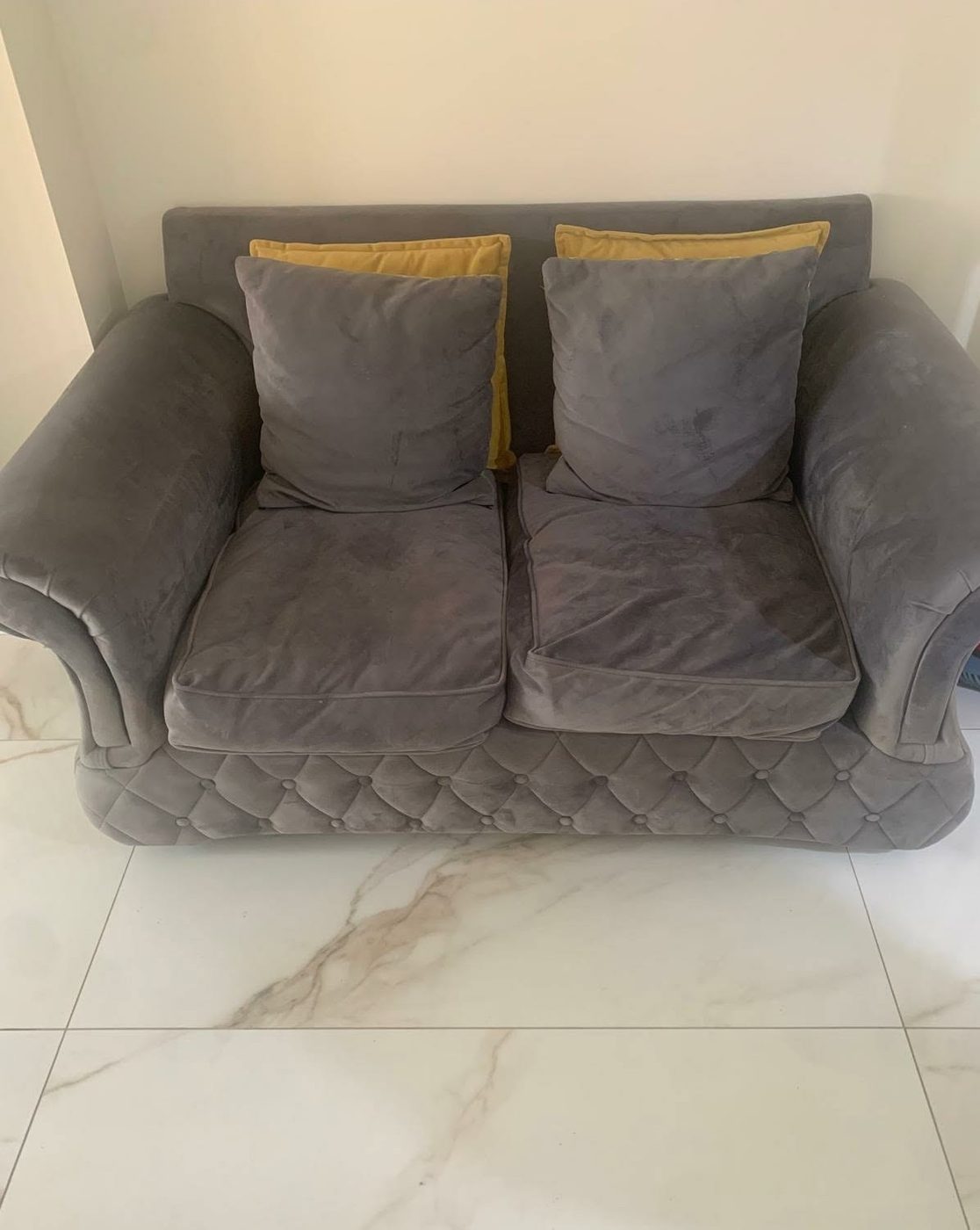 A grey two-seat sofa on a tiled floor, before