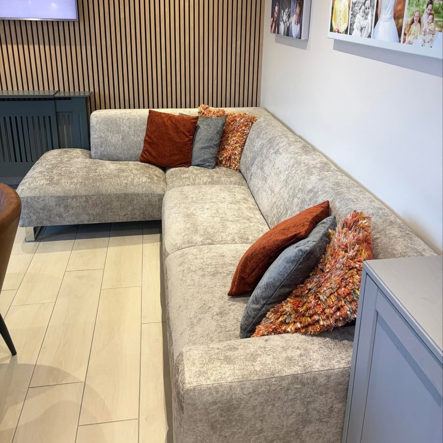 L-shaped grey sofa with rust, grey and patterned cushions in a room with slat wall panels