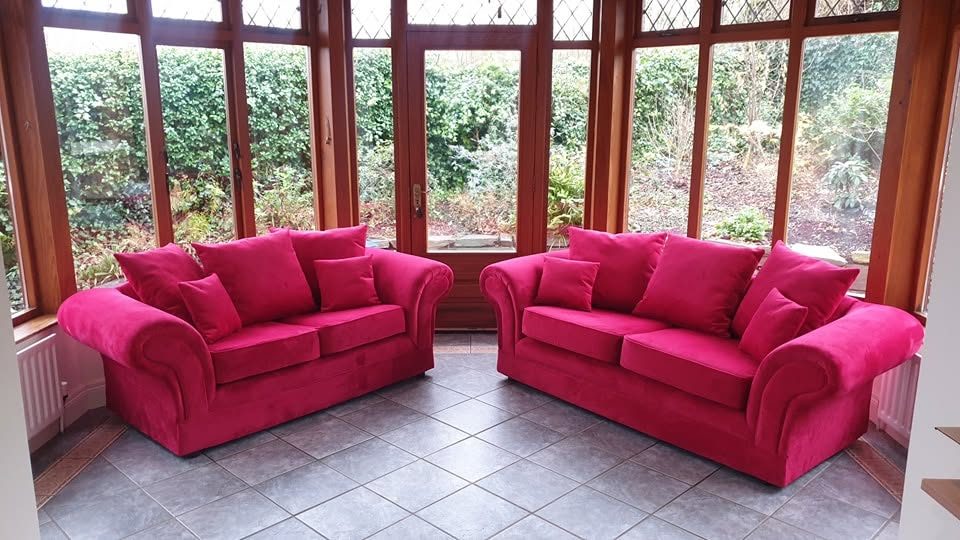 Two red sofas with cushions in a tiled room with wood-framed windows facing a garden